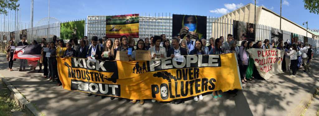 large group of people in protest, banners "Kick Industry Out" & "People Over Polluters"