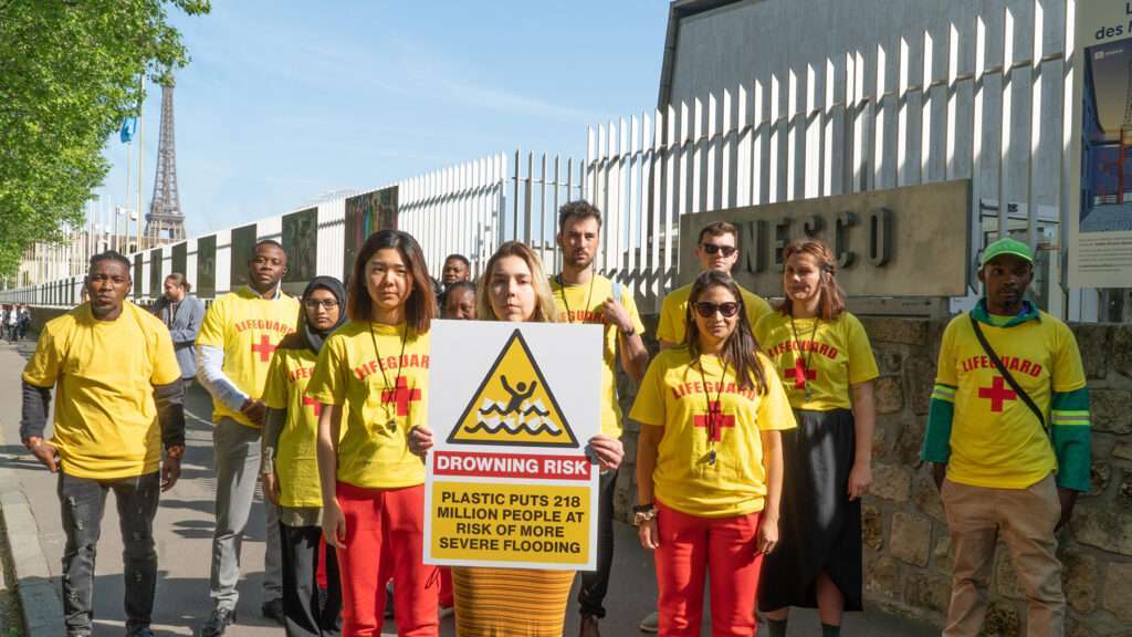 group of people in yellow lifeguard shirts, sign "Drowning Risk"