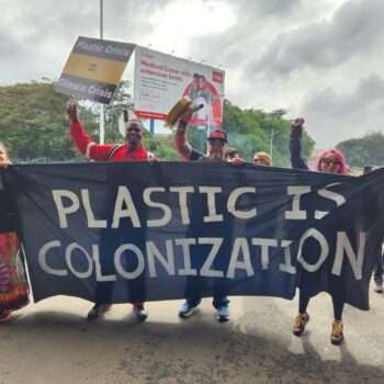 people marching with banner "Plastic is Colonization"