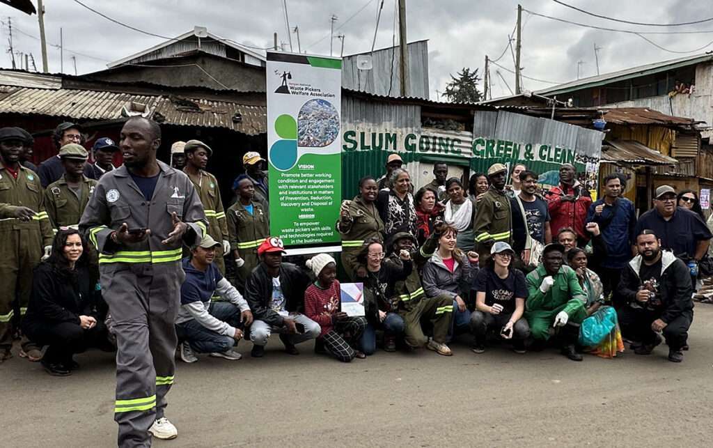 large group of people in front of sign "Slum going clean and green"